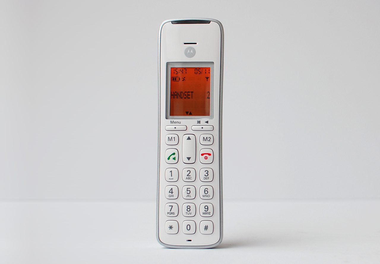 Promoting inclusivity through age-neutral design with SGW Global. Side view of the CD111 Telephone designed by Rodd for SGW GLOBAL.White handset on a pale grey backdrop illumintaed with an orange screen