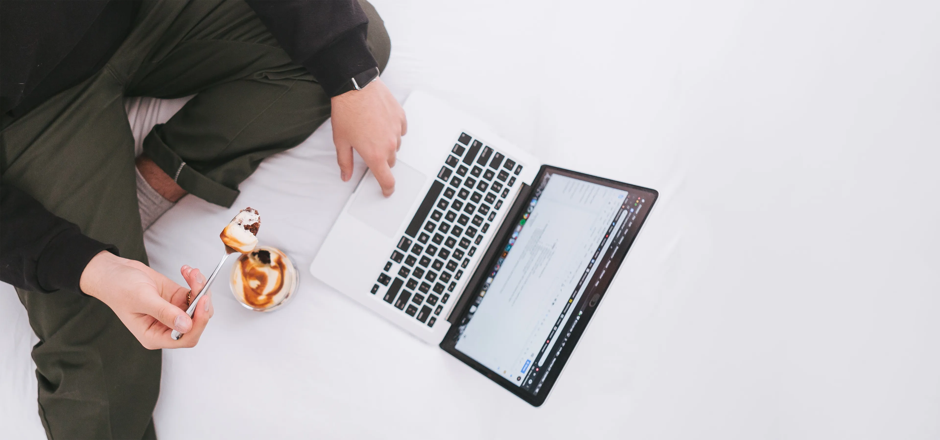 Man eating yoghurt while browsing on a laptop