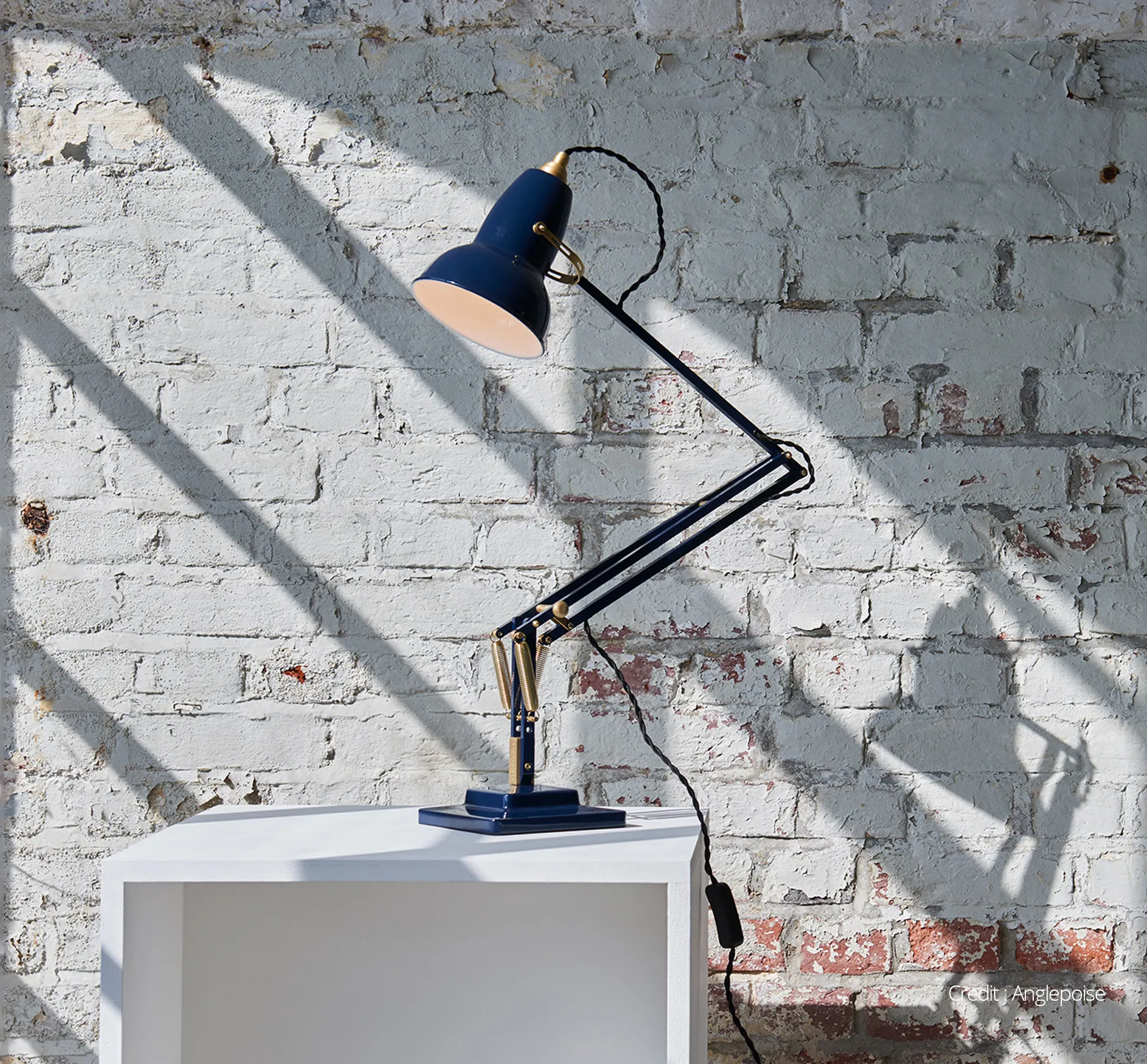 Anglepoise lamp on a white plinth with peeling painted brick background