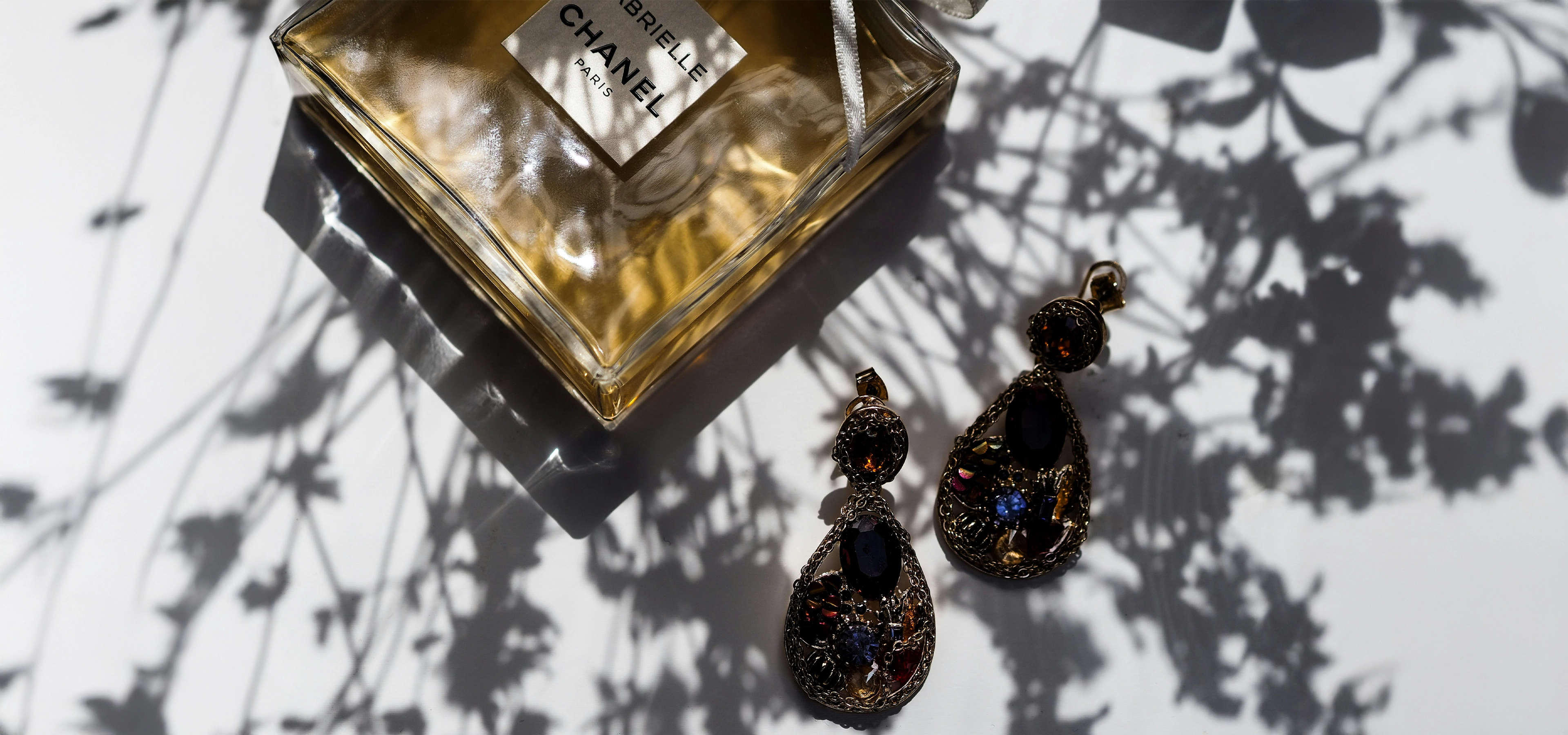 Jewellery and perfume on white table with a strong shadow of a plant