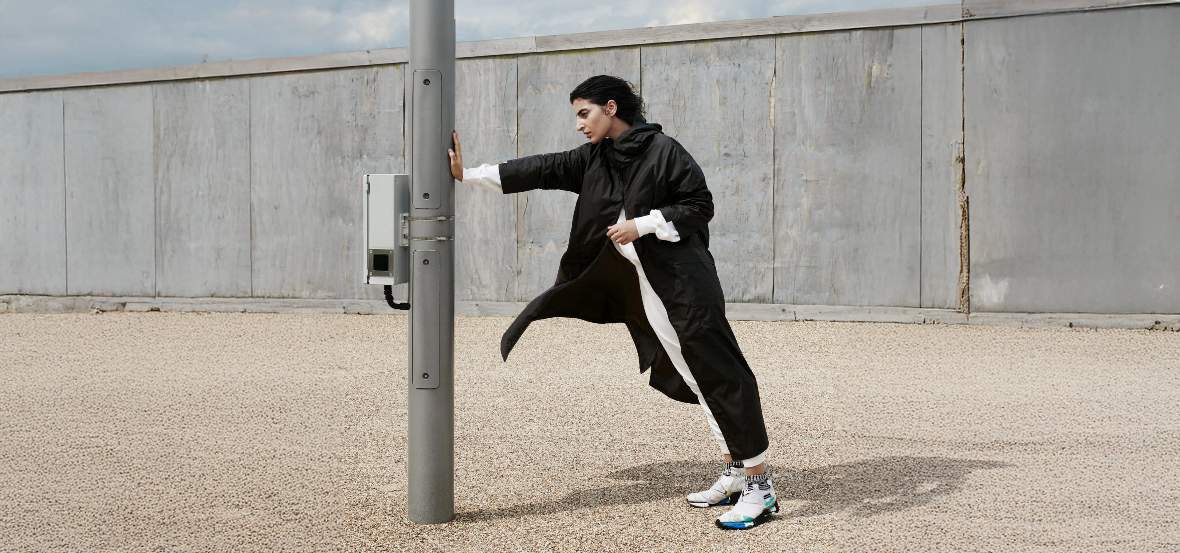 Person in a long black raincoat leaning against a lamppost