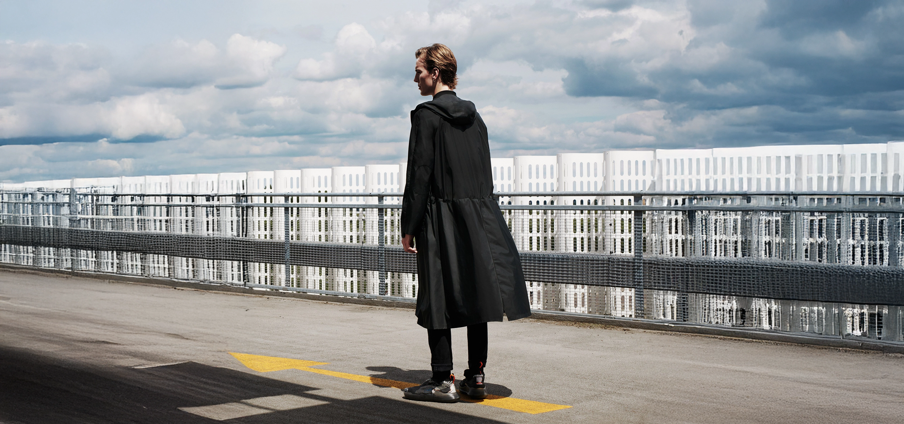 Man in long black raincoat stand in on a bridge