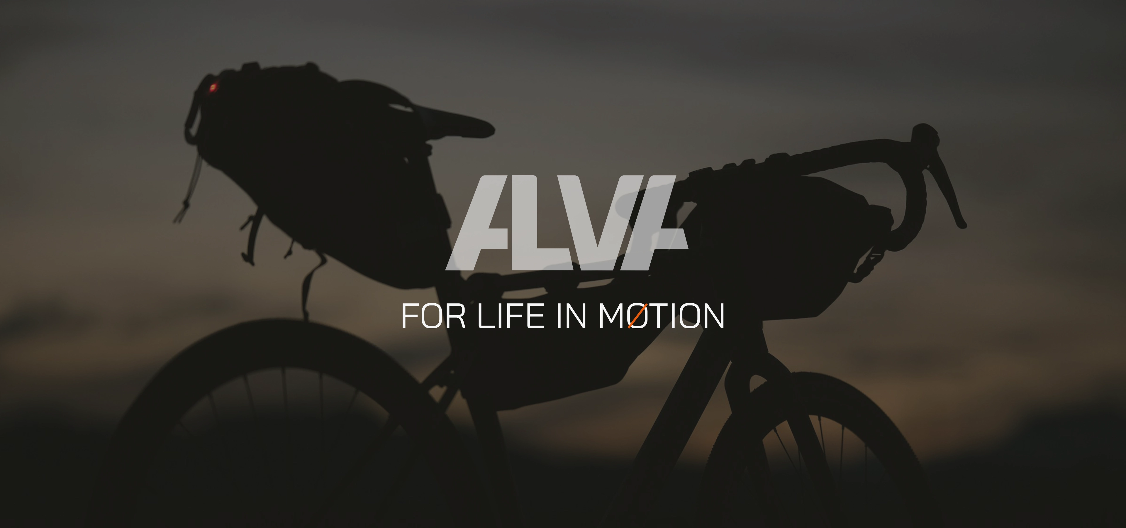 A branding mockup of a Alva torch logo hovering in front of a gravel bike in the landscape. The logo is white and the bike is in silhouette against a moodie sky. The second line of text reads a life in motion which is the branding line for the concept.